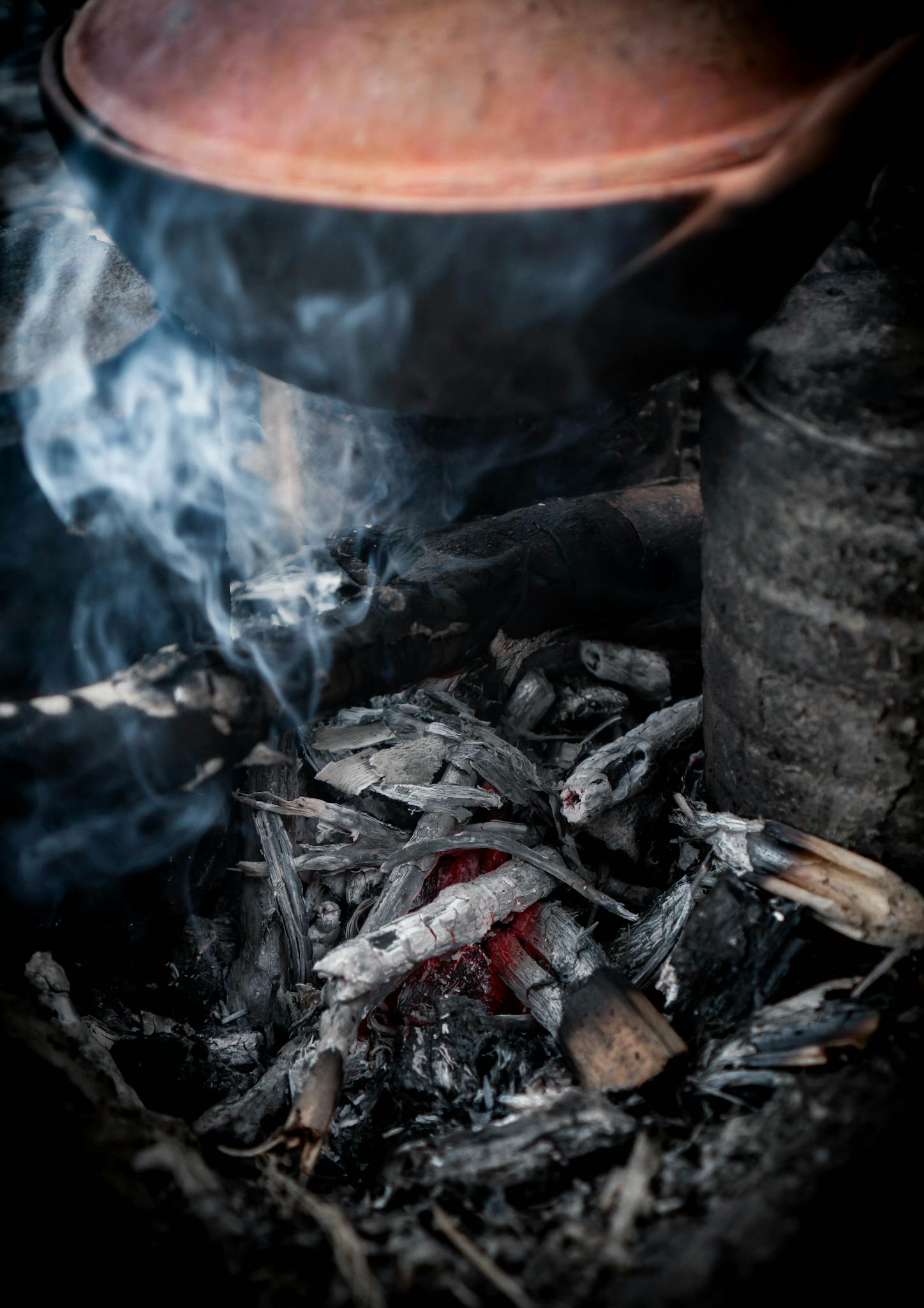 Close-up of a clay pot cooking over an open fire with smoke and embers.